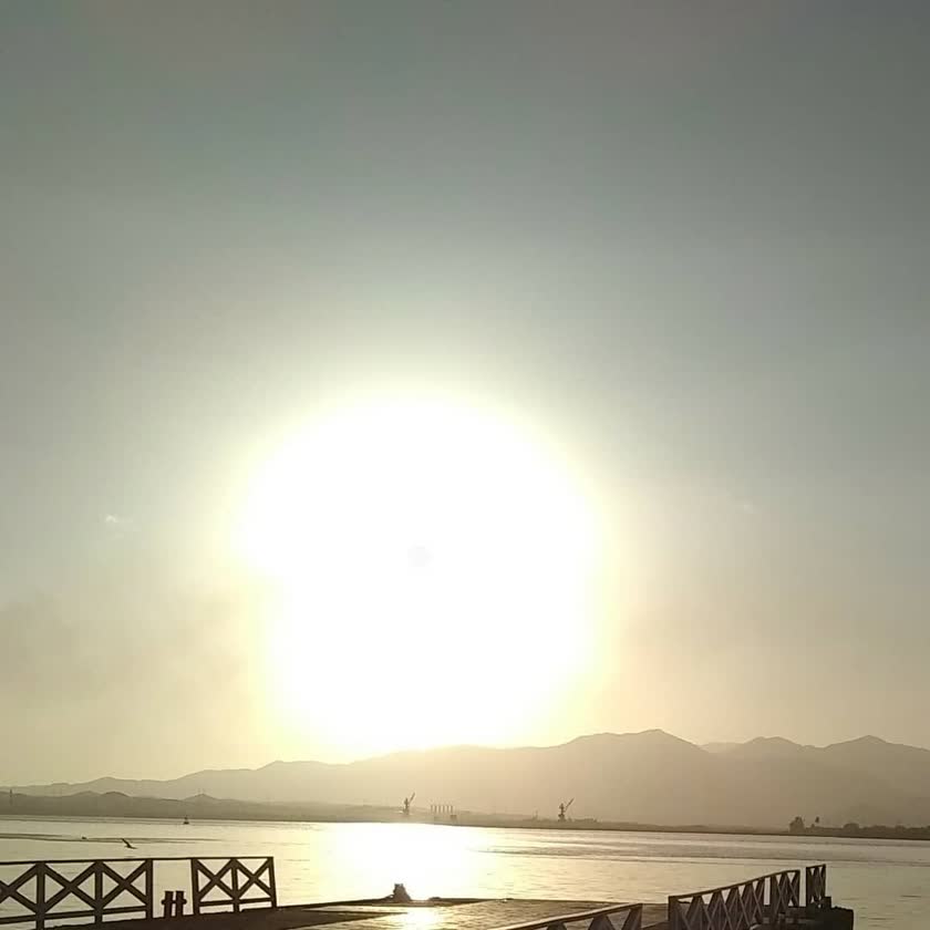 The sun setting over the water from a Cuban pier, mountains on the horizon, 2019