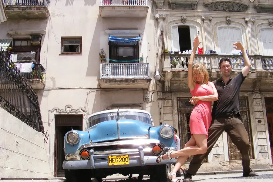 A couple dancing salsa in front of a classic car in Havana